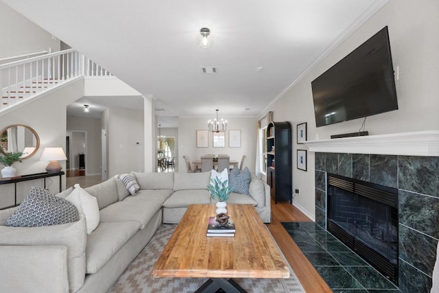 living room featuring visible vents, ornamental molding, a fireplace, wood finished floors, and a notable chandelier