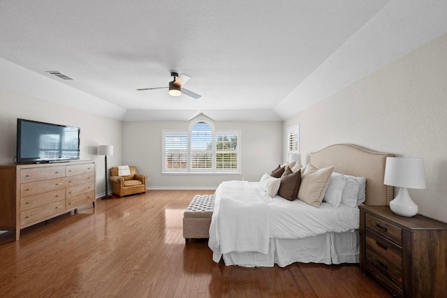 bedroom with wood finished floors, visible vents, baseboards, lofted ceiling, and ceiling fan