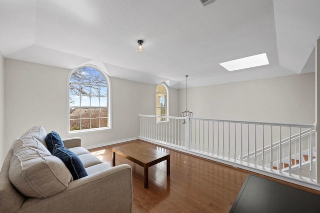 living area with baseboards, wood finished floors, and lofted ceiling with skylight