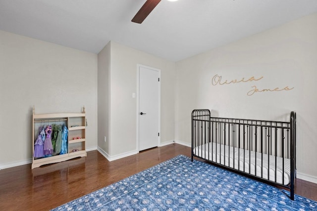 bedroom featuring a nursery area, wood finished floors, baseboards, and ceiling fan