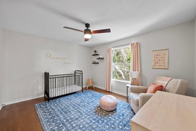 bedroom featuring ceiling fan, baseboards, a nursery area, and wood finished floors