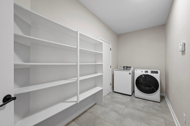 washroom featuring laundry area, light tile patterned floors, washing machine and dryer, and baseboards