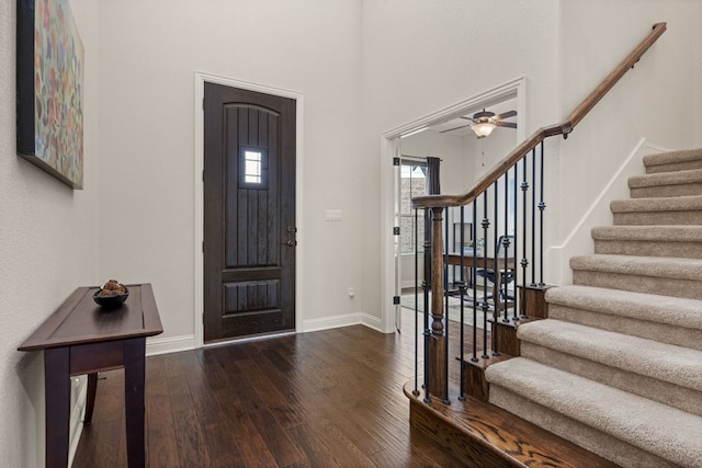 foyer with wood-type flooring, a towering ceiling, baseboards, and stairs