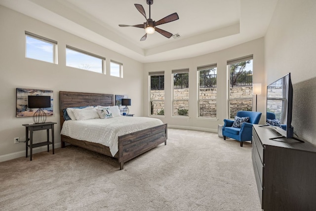 bedroom with light carpet, visible vents, a tray ceiling, and baseboards