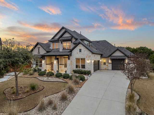 view of front facade with driveway, stone siding, roof with shingles, an attached garage, and stucco siding