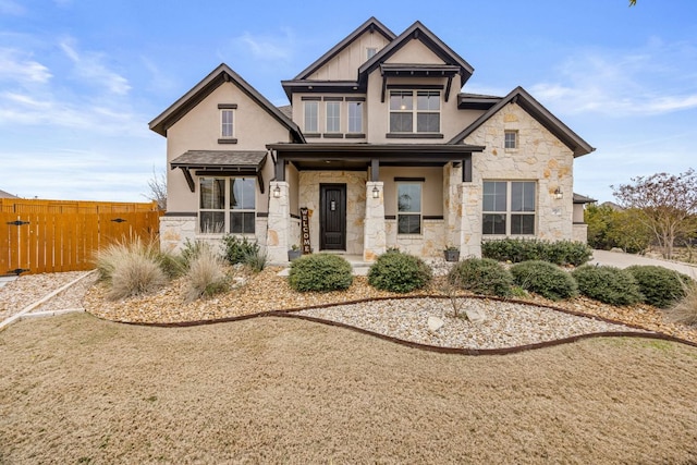 view of front of house with covered porch, fence, stone siding, stucco siding, and board and batten siding