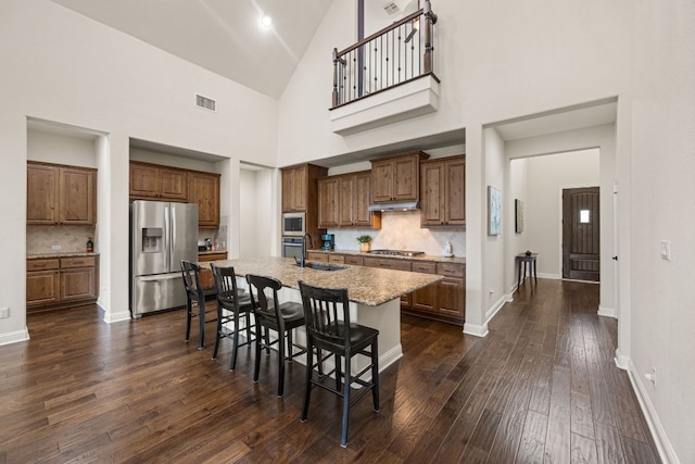 kitchen featuring stainless steel appliances, a breakfast bar, visible vents, dark wood-style floors, and a center island with sink