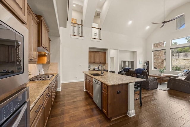 kitchen featuring a kitchen breakfast bar, open floor plan, stainless steel appliances, under cabinet range hood, and a sink