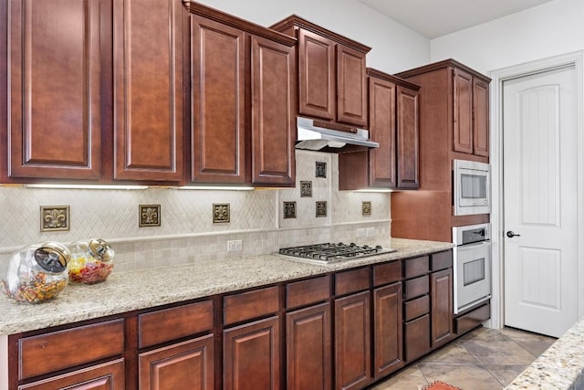 1428 Rowan Dr, Georgetown, TX 78628 - kitchen featuring appliances with stainless steel finishes, tasteful backsplash, under cabinet range hood, light stone counters, and light tile patterned floors