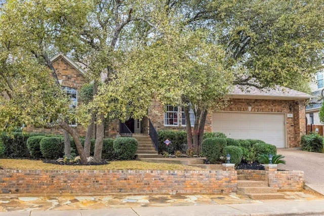 view of property hidden behind natural elements featuring an attached garage, driveway, and brick siding