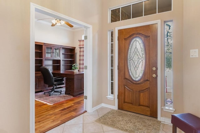 entryway featuring light tile patterned floors, ornamental molding, a ceiling fan, and baseboards