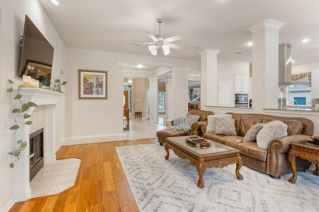 living room with decorative columns, a ceiling fan, light wood-type flooring, baseboards, and a tile fireplace