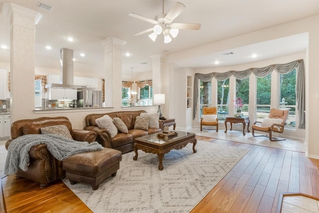 living room featuring ceiling fan, wood finished floors, visible vents, and ornate columns