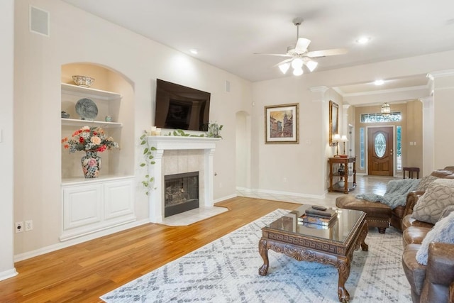 living room featuring built in shelves, visible vents, a tiled fireplace, wood finished floors, and baseboards