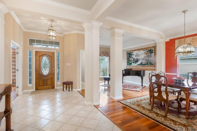 foyer entrance featuring light tile patterned floors, decorative columns, baseboards, crown molding, and a chandelier