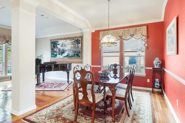 dining space with a chandelier, wood finished floors, crown molding, and decorative columns