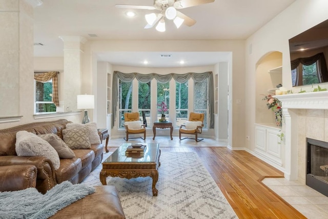 living area featuring ceiling fan, a tile fireplace, visible vents, and light wood-style floors