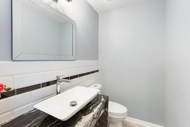 half bathroom featuring tile patterned flooring, a sink, tile walls, and toilet