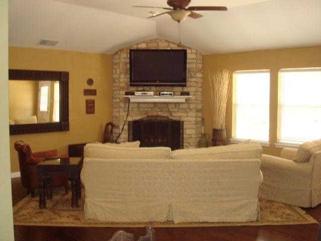 living area featuring a large fireplace, ceiling fan, lofted ceiling, and visible vents