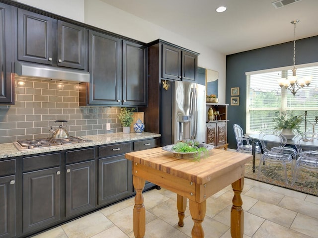 kitchen featuring under cabinet range hood, appliances with stainless steel finishes, light stone countertops, tasteful backsplash, and decorative light fixtures