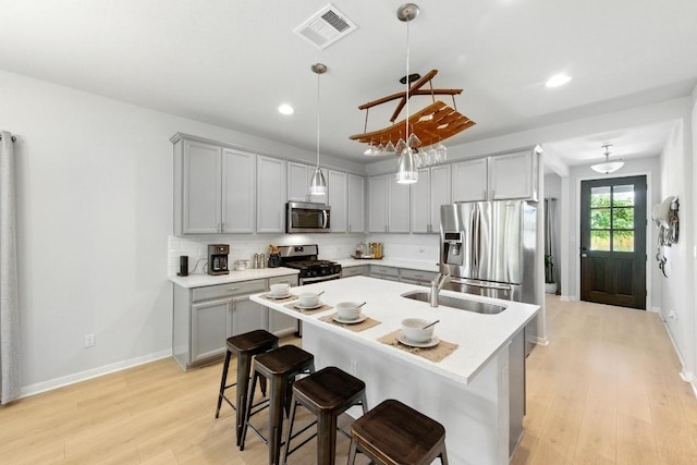 107 Trailside Ln, Bastrop, TX 78602 - kitchen featuring appliances with stainless steel finishes, gray cabinetry, light wood finished floors, a sink, and tasteful backsplash