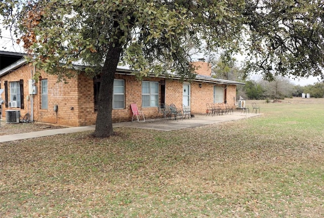 rear view of house featuring central AC unit, brick siding, a lawn, a chimney, and a patio area