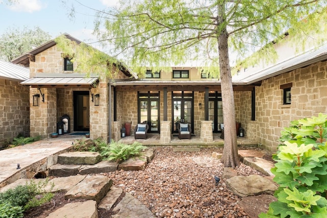 back of property featuring a patio area, metal roof, a standing seam roof, and stone siding