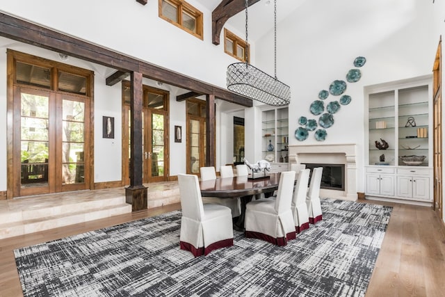 dining space with a towering ceiling, built in shelves, wood finished floors, and a glass covered fireplace