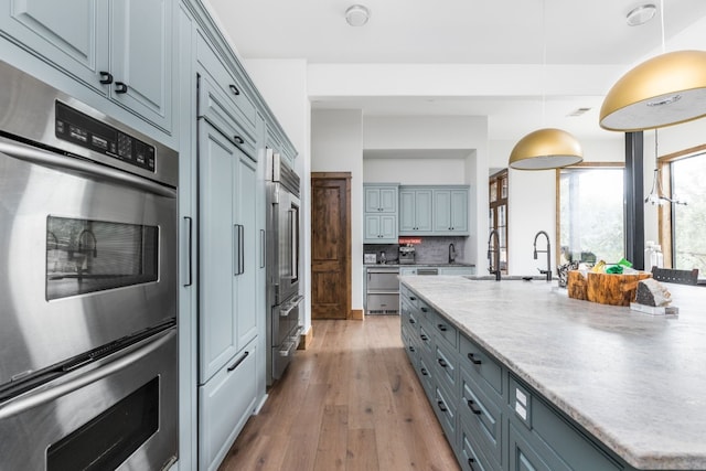 kitchen with backsplash, gray cabinetry, double oven, a sink, and light wood-type flooring