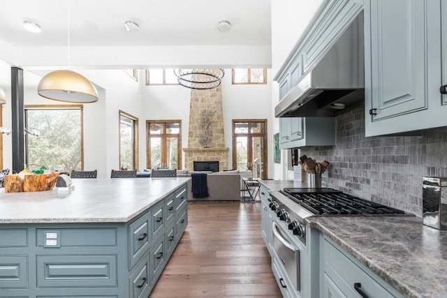 kitchen featuring wood finished floors, hanging light fixtures, under cabinet range hood, a fireplace, and backsplash