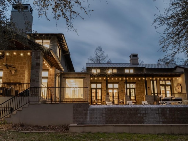 rear view of property with a standing seam roof, a chimney, metal roof, and stone siding