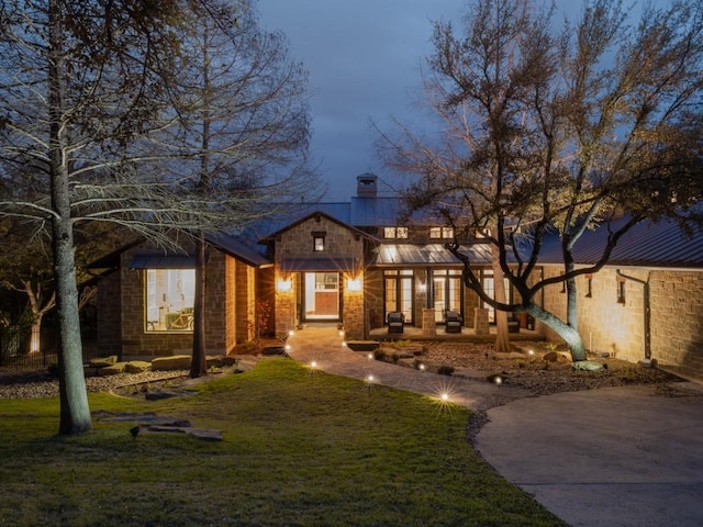 view of front facade featuring metal roof, driveway, a chimney, and a front yard