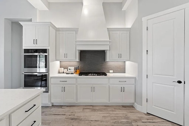 kitchen featuring custom exhaust hood, light countertops, stainless steel double oven, white cabinetry, and black gas stovetop