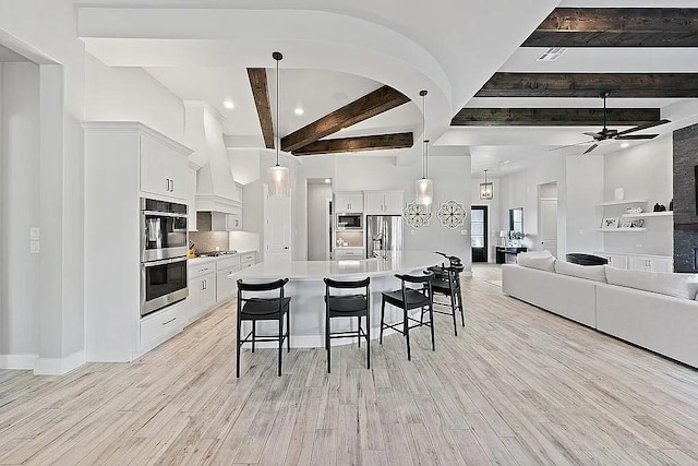 kitchen featuring light wood-style flooring, appliances with stainless steel finishes, white cabinetry, premium range hood, and a kitchen breakfast bar