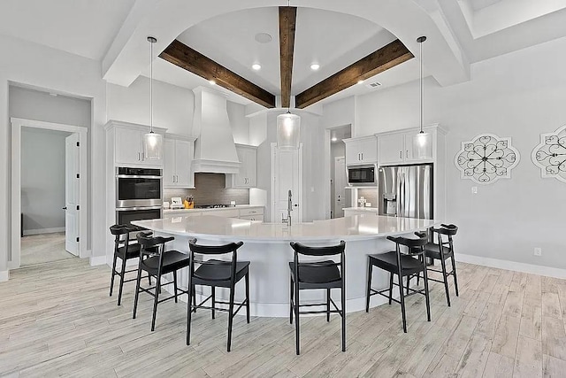 kitchen with light wood-style floors, light countertops, appliances with stainless steel finishes, tasteful backsplash, and custom range hood