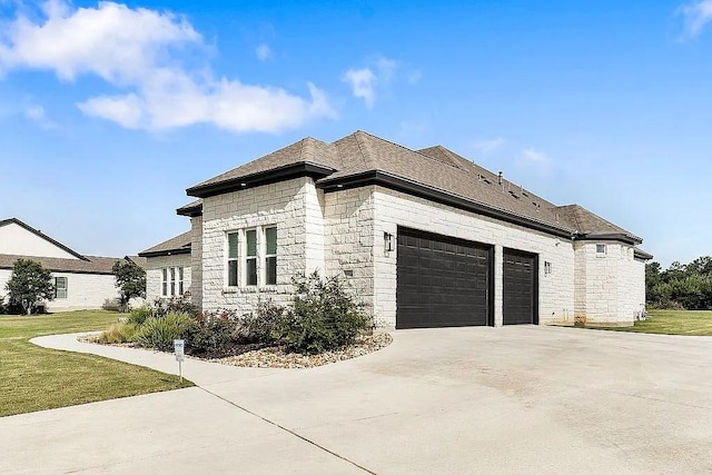 view of side of property featuring stone siding, concrete driveway, a yard, and an attached garage