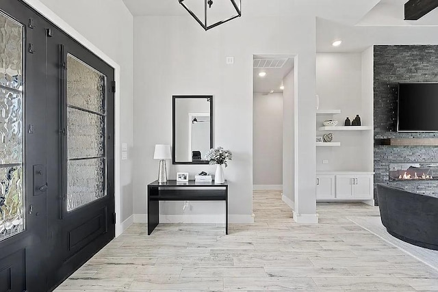 foyer entrance with a stone fireplace, light wood finished floors, visible vents, and baseboards