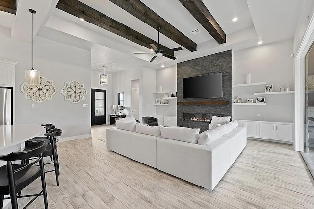 living room with beam ceiling, a fireplace, visible vents, light wood-style floors, and baseboards