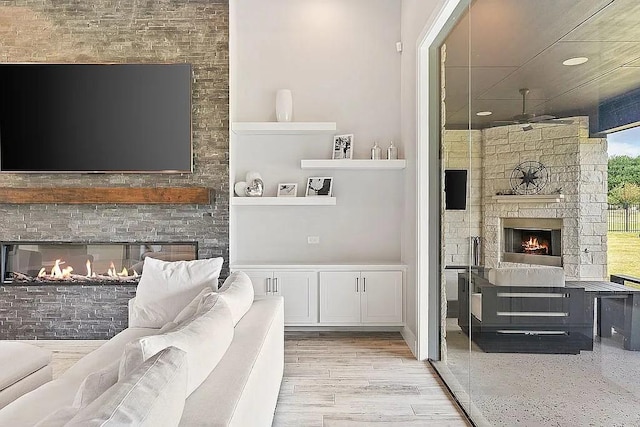 living area featuring a lit fireplace, wood finished floors, and a ceiling fan