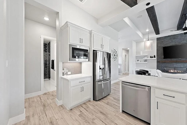 kitchen featuring light wood finished floors, white cabinets, stainless steel appliances, light countertops, and beam ceiling