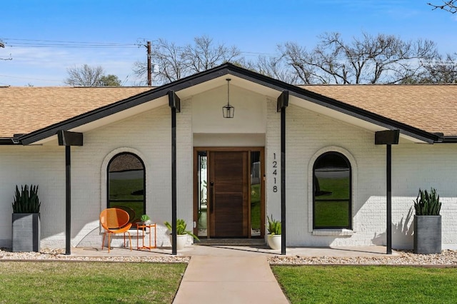 view of exterior entry with brick siding and roof with shingles