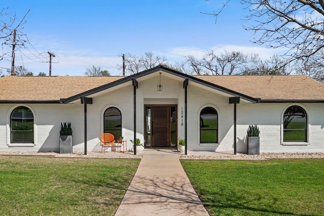 view of front of property with a shingled roof, a front lawn, and brick siding