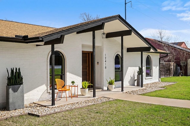 exterior space with brick siding, a yard, and roof with shingles