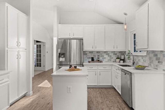 kitchen with a sink, a center island, vaulted ceiling, appliances with stainless steel finishes, and decorative backsplash