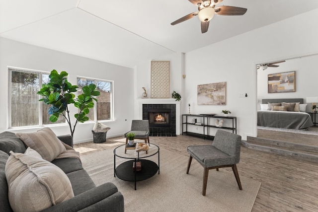 living room with baseboards, ceiling fan, a tiled fireplace, and wood finished floors