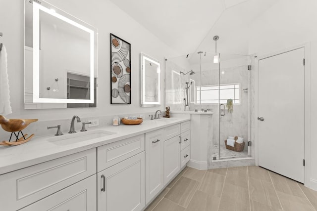 bathroom featuring a stall shower, vaulted ceiling, a sink, and double vanity