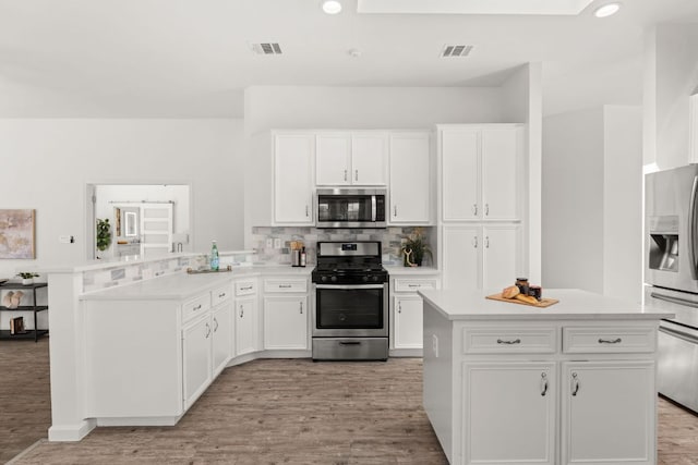 kitchen featuring stainless steel appliances, a peninsula, backsplash, and light countertops