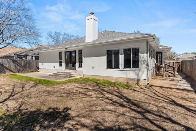 rear view of house featuring a fenced backyard, a shingled roof, french doors, a chimney, and a patio area