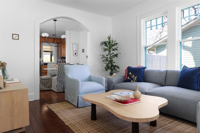 living room with dark wood-style floors, arched walkways, and crown molding