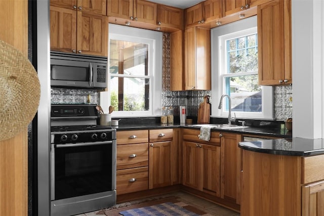 kitchen featuring a sink, brown cabinetry, black gas range, and a wealth of natural light